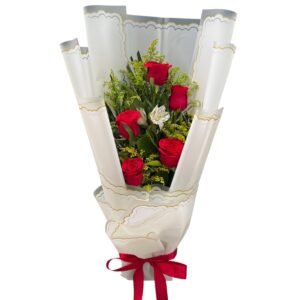 Bouquet of red roses with yellow filler flowers wrapped in white ornate paper with gold trim and a red ribbon at the base.
