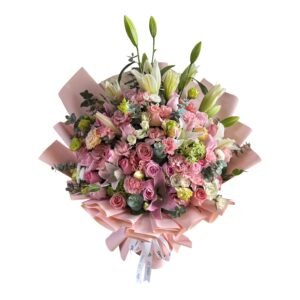 Bouquet of pink roses, carnations, and lilies with greenery wrapped in pink paper and a white ribbon.